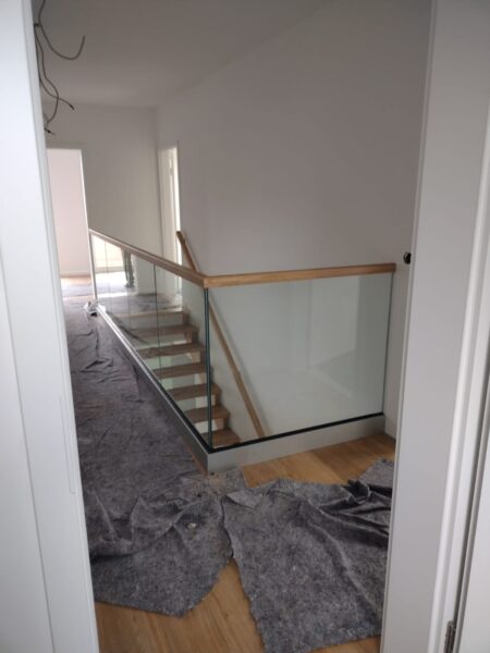 Glasbrüstung mit Holzhandlauf am oberen Treppenpodest während der Bauphase
