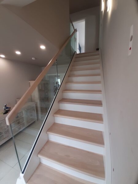 Holztreppe mit weißen Setzstufen, Glasgeländer und Holzhandlauf