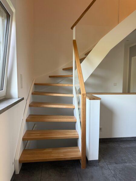 Holztreppe neben einem Fenster mit Glasgeländer und Holzhandlauf