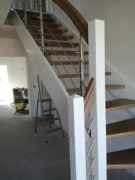 Holztreppe mit weißen Pfosten und Edelstahlgeländer während der Montage