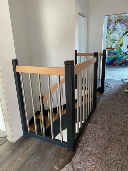 Dunkle Geländerpfosten mit hellen Stäben und Holzhandlauf an einer Treppenöffnung