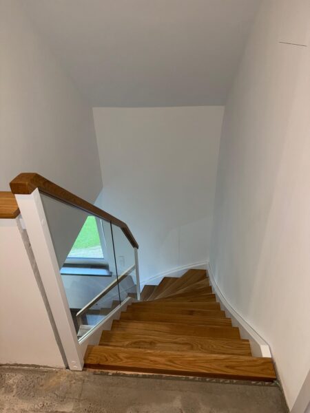 Blick von oben auf eine gewendelte Holztreppe mit Glasgeländer