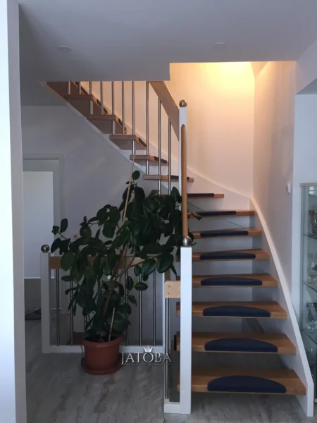 Holztreppe mit hellen Stufen, weißen Pfosten und dunklen Stufenmatten
