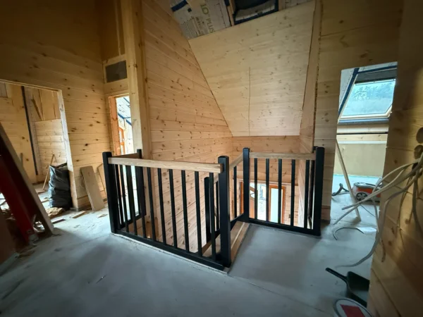 Dunkles Geländer mit Holzhandlauf an einer Treppenöffnung im Holzhaus