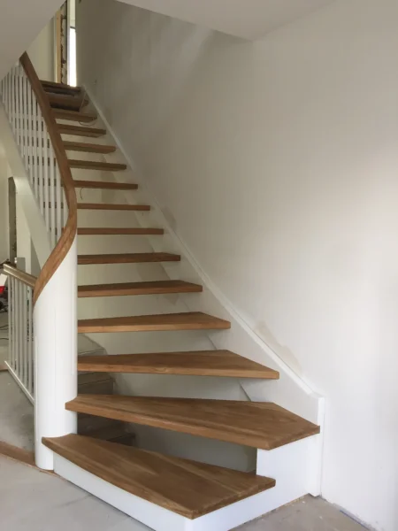 Gebogene Holztreppe mit weißer Wange und geschwungenem Holzhandlauf