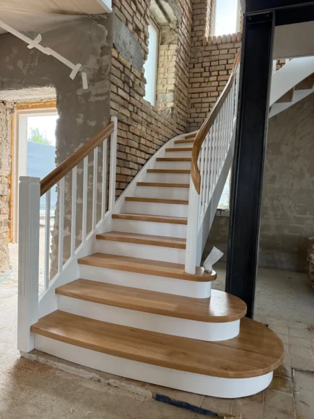 Gebogene Holztreppe mit weißer Wange und geschwungenem Holzhandlauf