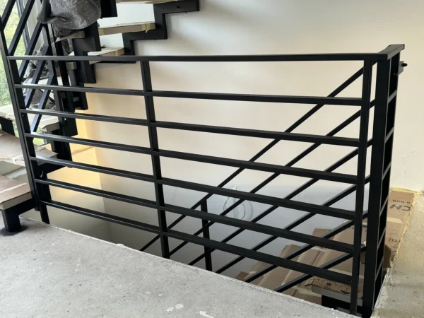 Schwarzes Metallgeländer am Podest einer Treppe mit Metallwangen