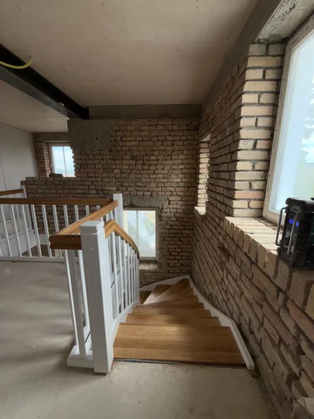 Blick von oben auf eine Holztreppe im Rohbau mit weißen Geländerstäben