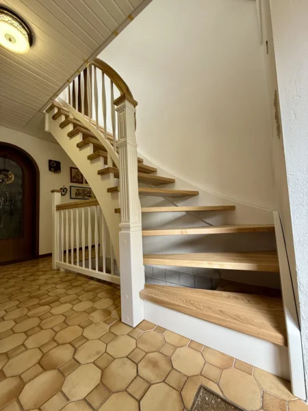 Gebogene Holztreppe mit weißer Wange und geschwungenem Holzhandlauf