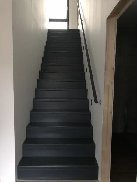Gerade Treppe mit dunklem Stufenbelag zwischen weißen Wänden