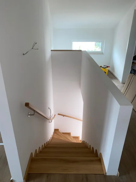 Blick von oben auf eine Holztreppe zwischen weißen Wänden