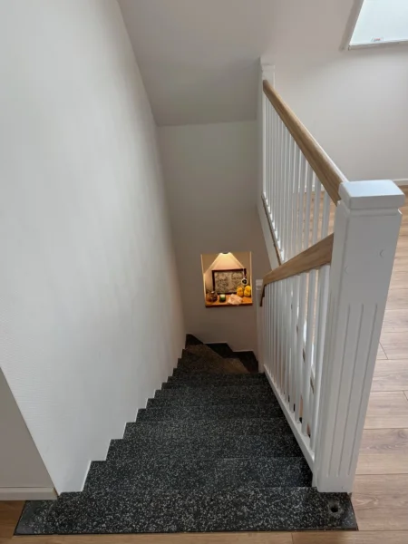 Treppe mit grauem Stufenbelag und weißem Geländer mit Holzhandlauf